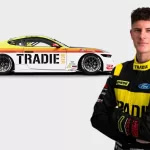Declan Fraser in his motorsport racing suit with arms crossed standing in fron tof his supercar